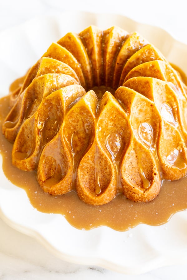 A brown sugar caramel pound cake on a white platter, baked in a bundt pan and topped with caramel sauce.