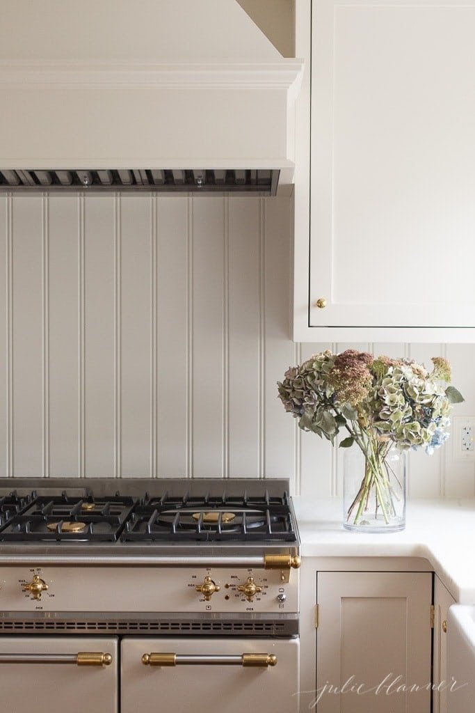 A white kitchen with a bead board backsplash, vase of flowers on the counter.