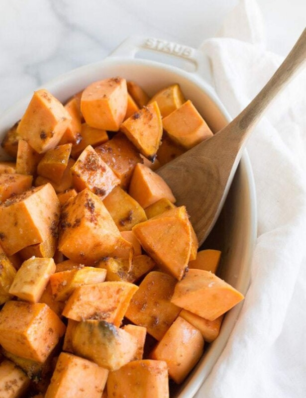 wood spoon in casserole dish filled with roasted sweet potatoes