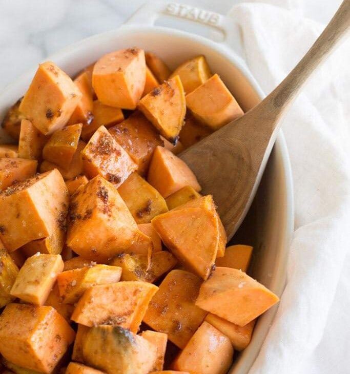 wood spoon in casserole dish filled with roasted sweet potatoes