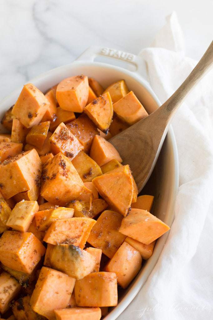 wood spoon in casserole dish filled with roasted sweet potatoes