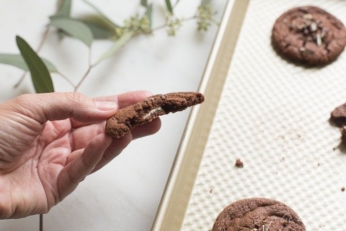 hand holding andes mint cookie split in half with chocolate cookies on baking sheet in background