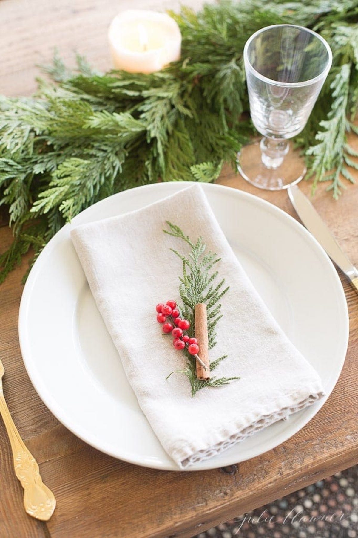 A Christmas table setting with a napkin, fork, and a sprig of holly amidst a garland.