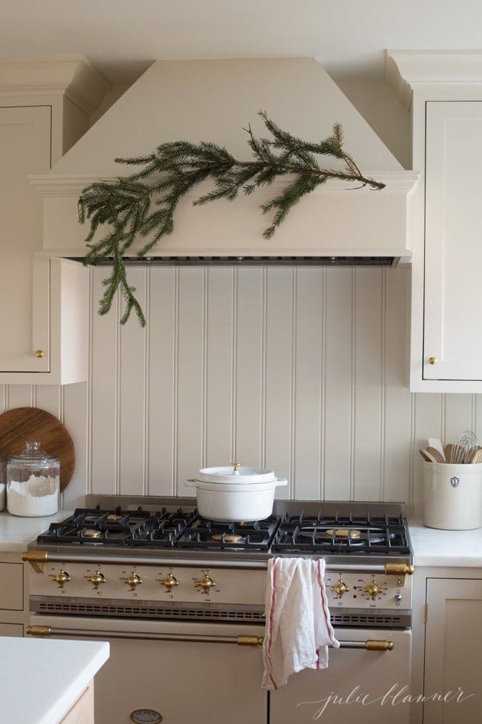A piece of evergreen on the hood of a range in a cream kitchen, for a natural christmas decor idea.