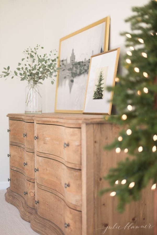A wooden dresser with a Christmas tree adorned with Christmas lights in front of it.