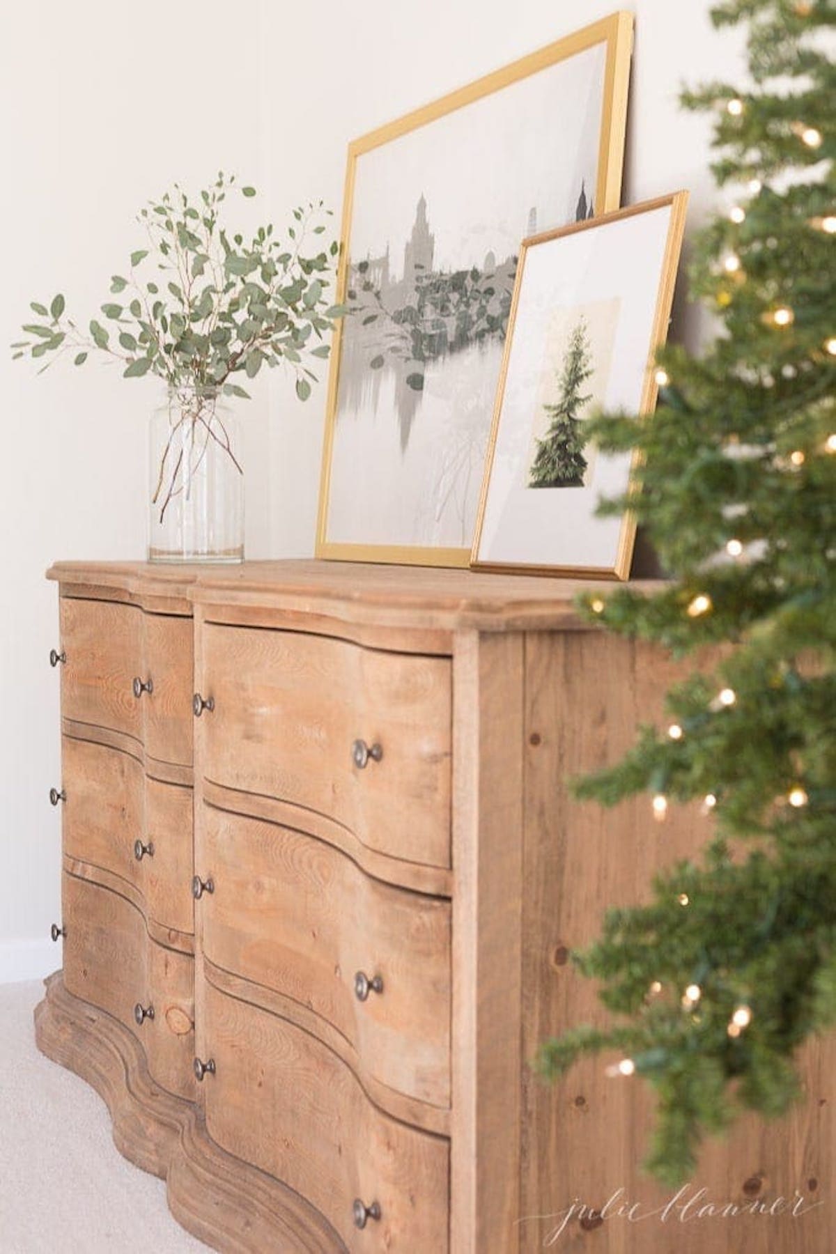 A wooden dresser adorned with a festive christmas tree, with twinkling Christmas lights illuminating the bedroom.