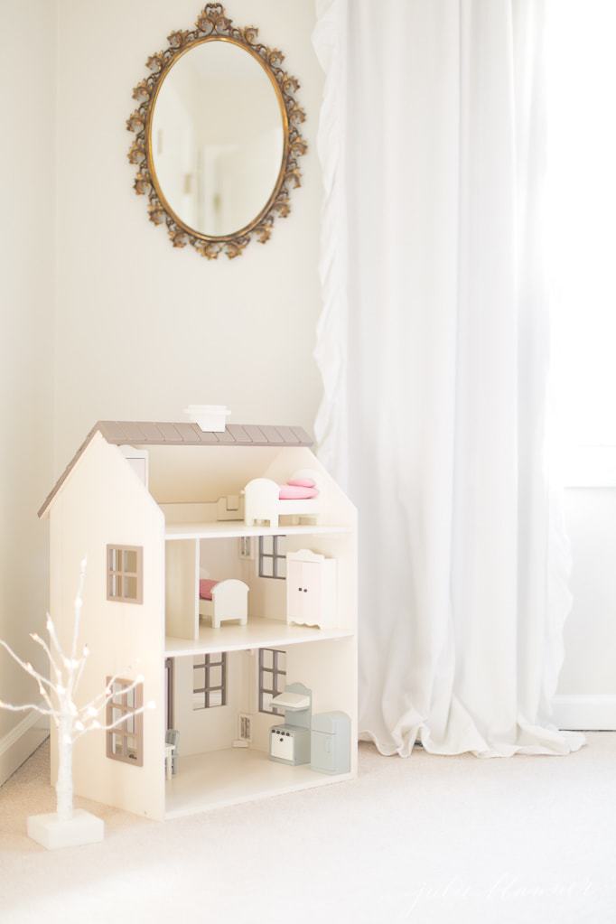 A little girl's room with a dollhouse and a small birch fairy light tree