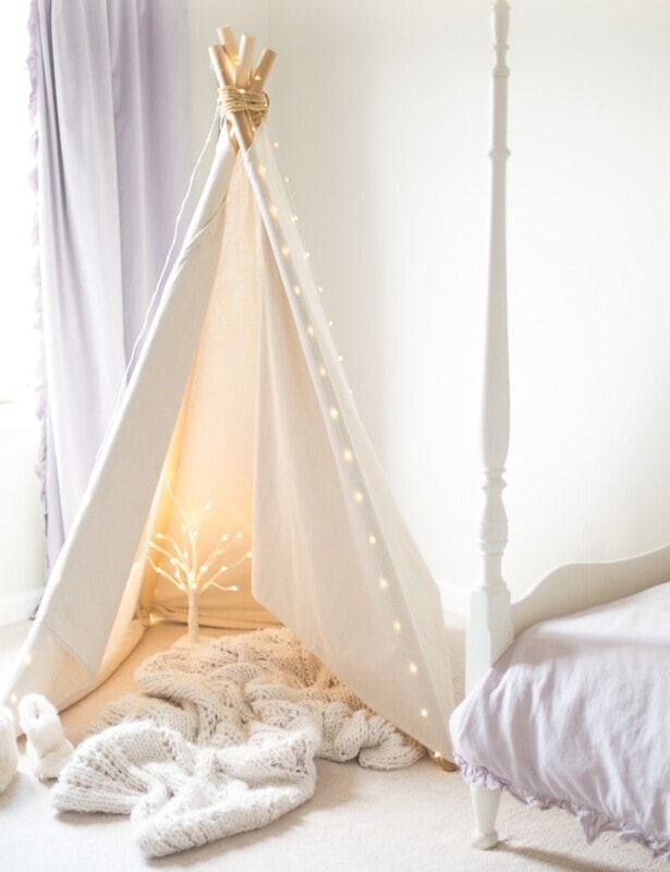 A white teepee in a child's white bedroom, with a white birch fairy light tree inside