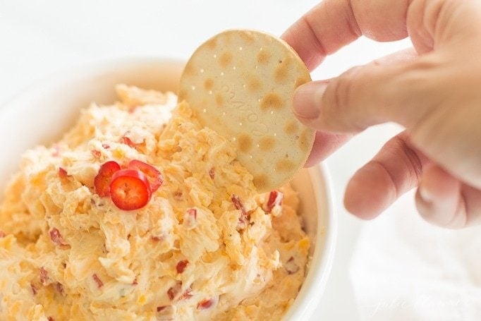 cracker being dipped into pimento cheese recipe in a white bowl