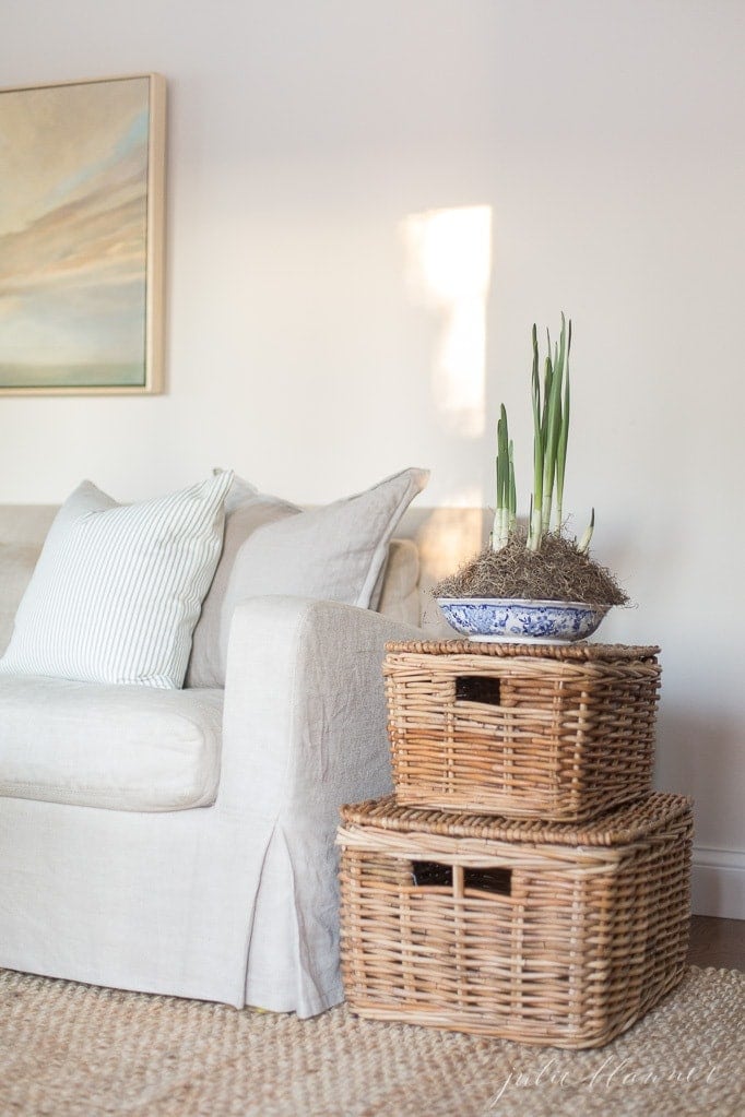 a family room with a linen sofa, sisal rug and stacked lidded baskets as a space saving furniture side table idea
