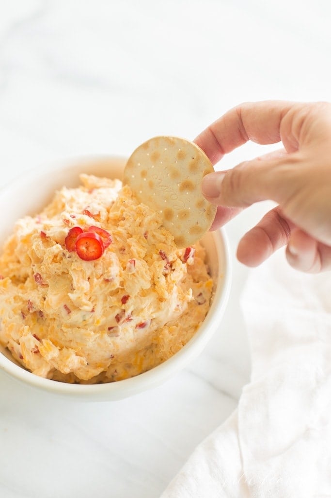 cracker being dipped into pimento cheese recipe in a white bowl