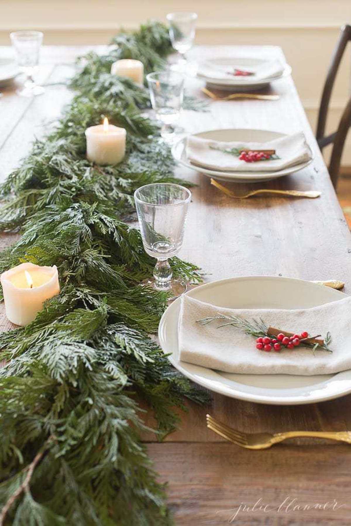 A Christmas table runner featuring garland adorned with greenery and pine cones.
