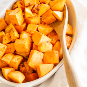 A white oval baking dish filled with roasted sweet potatoes.