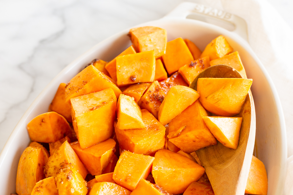 A white oval baking dish filled with roasted sweet potatoes. 