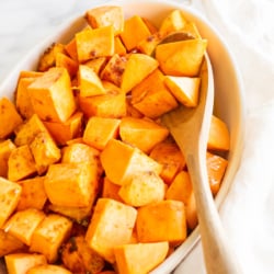 A white oval baking dish filled with roasted sweet potatoes.
