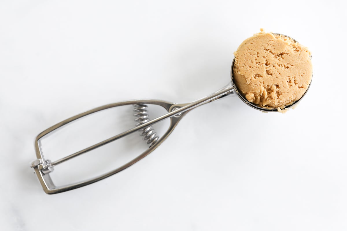 A metal spoon with a scoop of peanut butter on it, perfect for making stuffed peanut butter cookies.