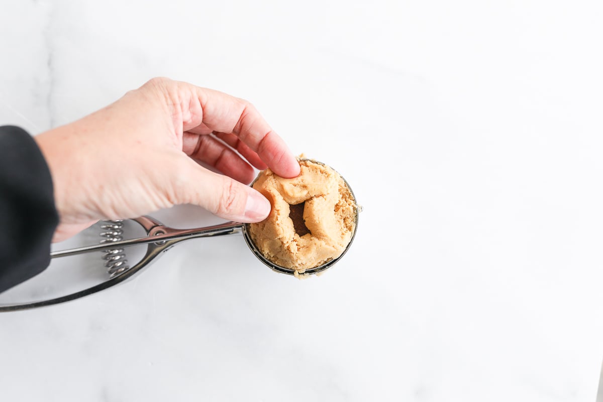 A person stuffing a peanut butter cookie with creamy peanut butter.