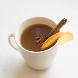 spiked apple cider in cream mug with orange slice cinnamon stick and star of anise