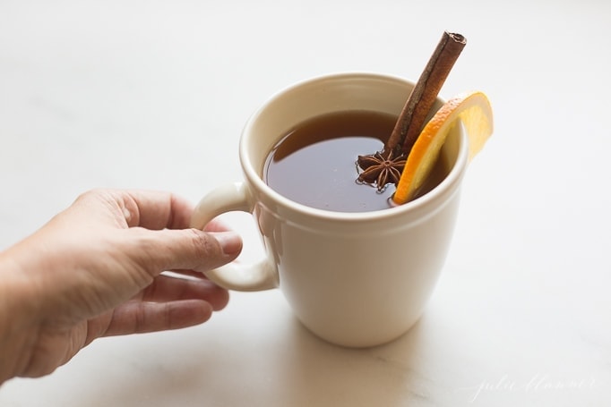 Spiked apple cider in a white mug, garnished with an orange slice, star anise, and cinnamon stick. 