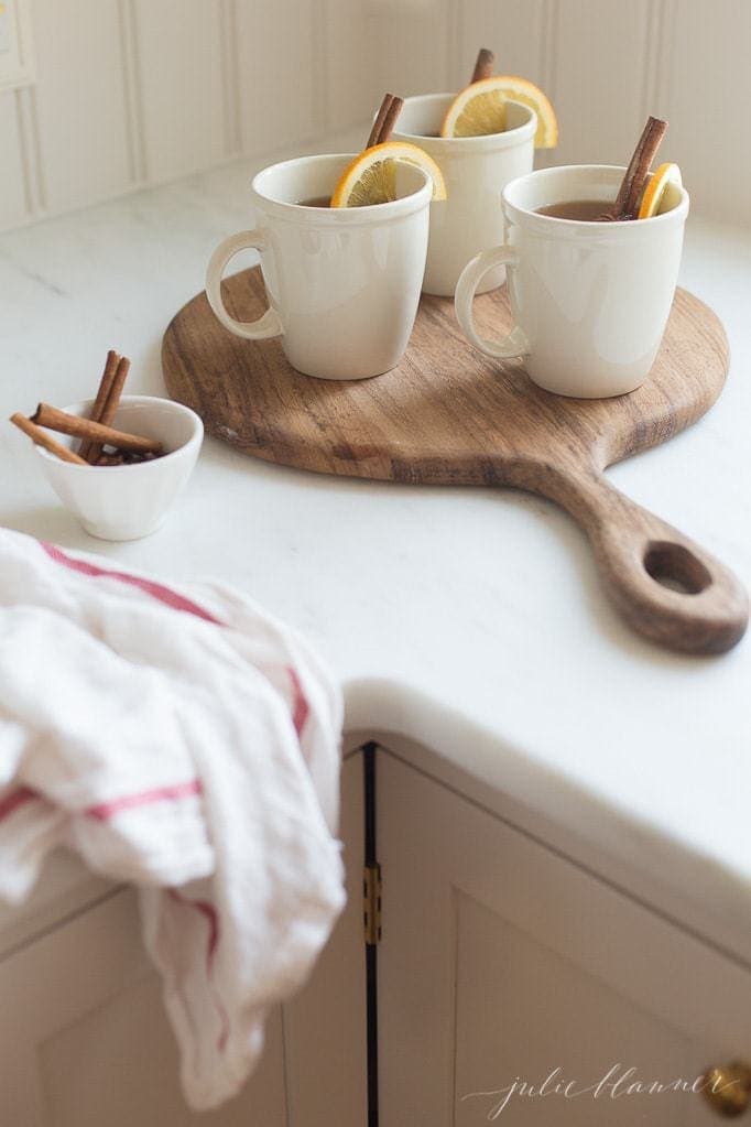 Spiked apple cider in white mugs on a wooden tray on a white countertop. 