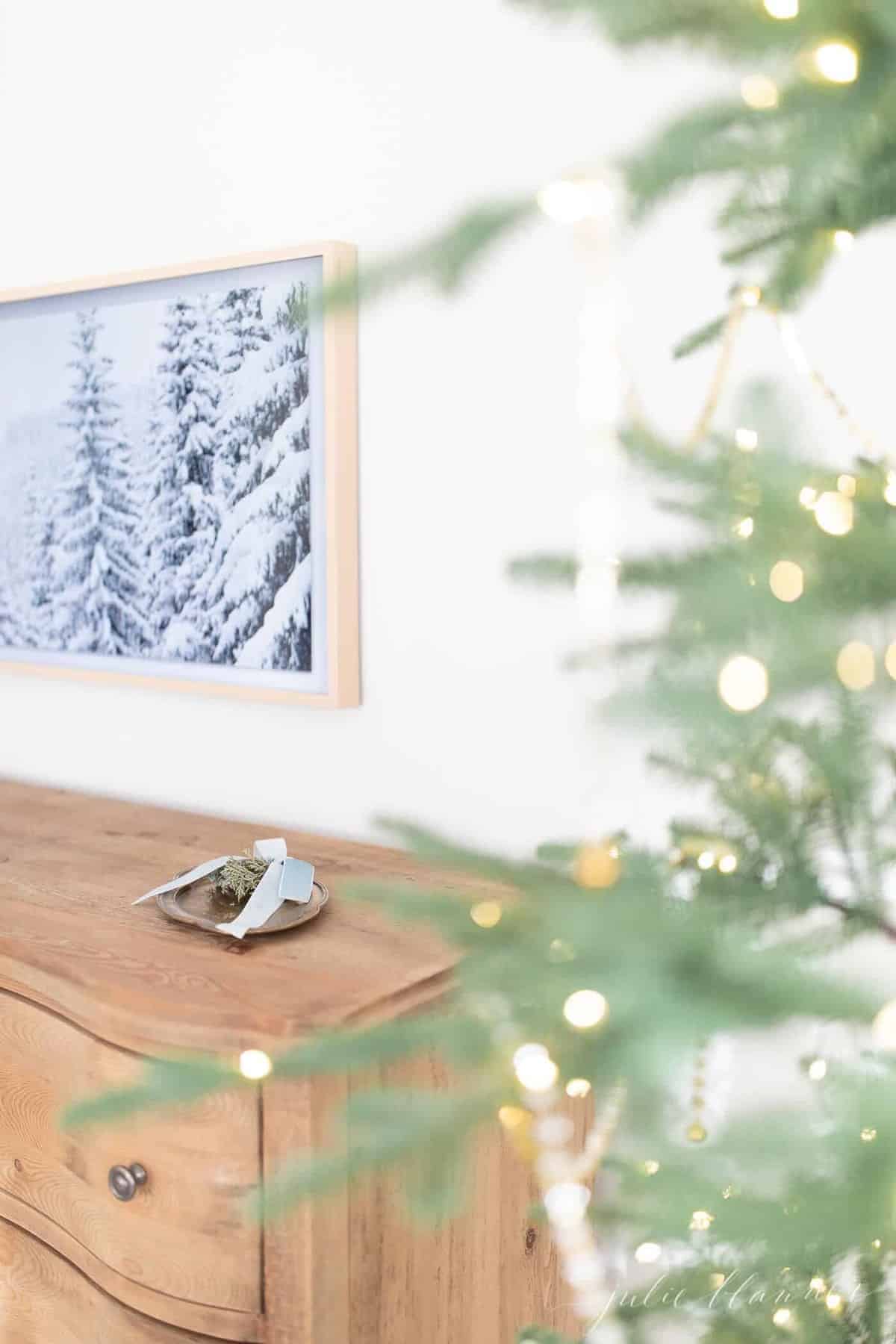 A Samsung art tv on the wall of a bedroom with a winter scene displayed, Christmas tree in foreground.