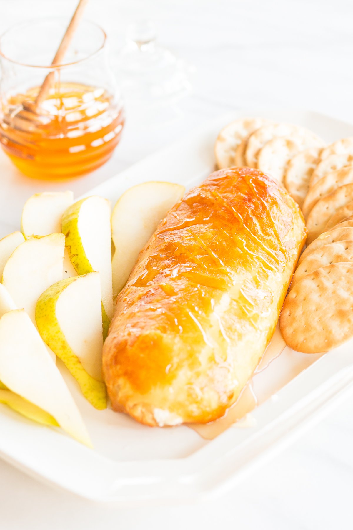 Baked goat cheese topped with honey with sliced pears and crackers for serving.
