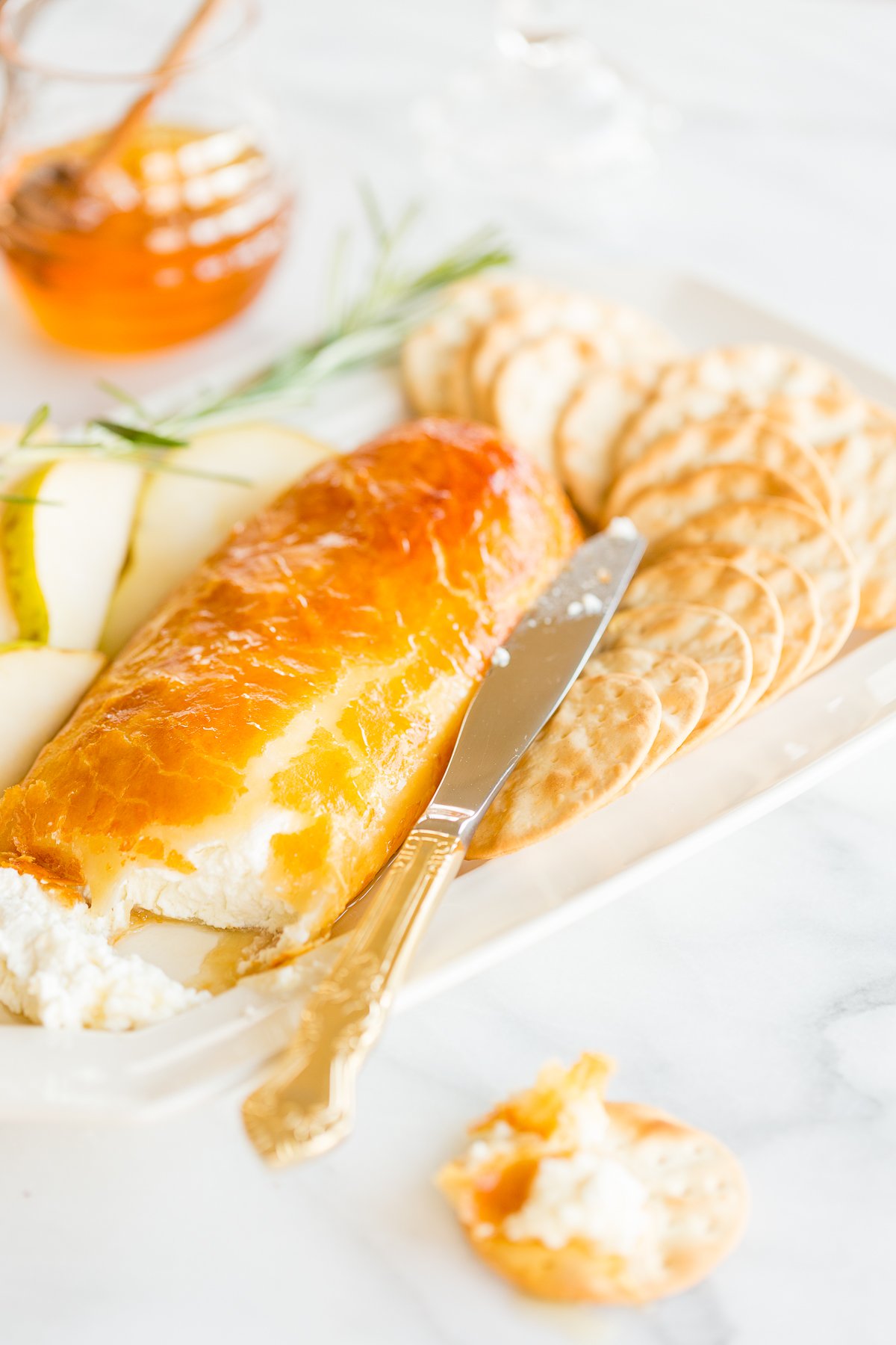 Baked goat cheese topped with honey with sliced pears and crackers for serving.