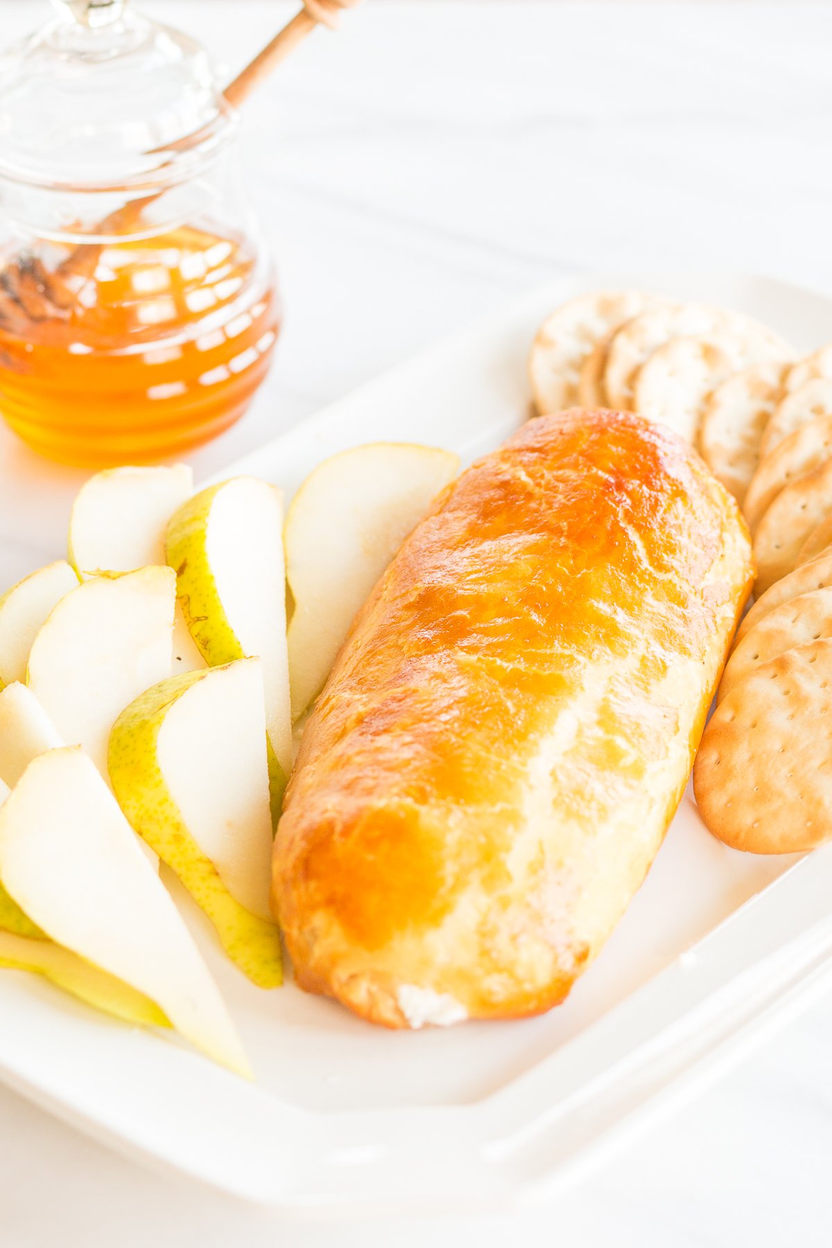 Baked goat cheese topped with honey with sliced pears and crackers for serving.