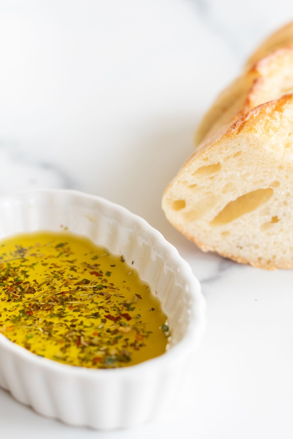A white ramekin full of olive oil bread dip, loaf of bread to the side. 