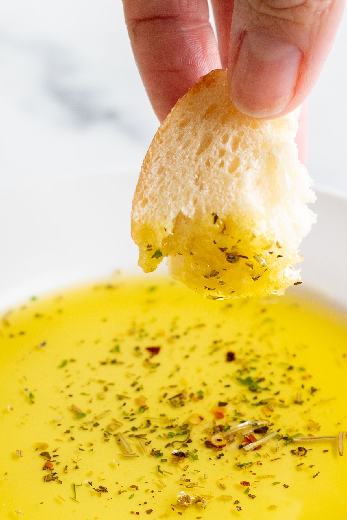 A hand dipping a piece of bread onto a plate of olive oil bread dip.