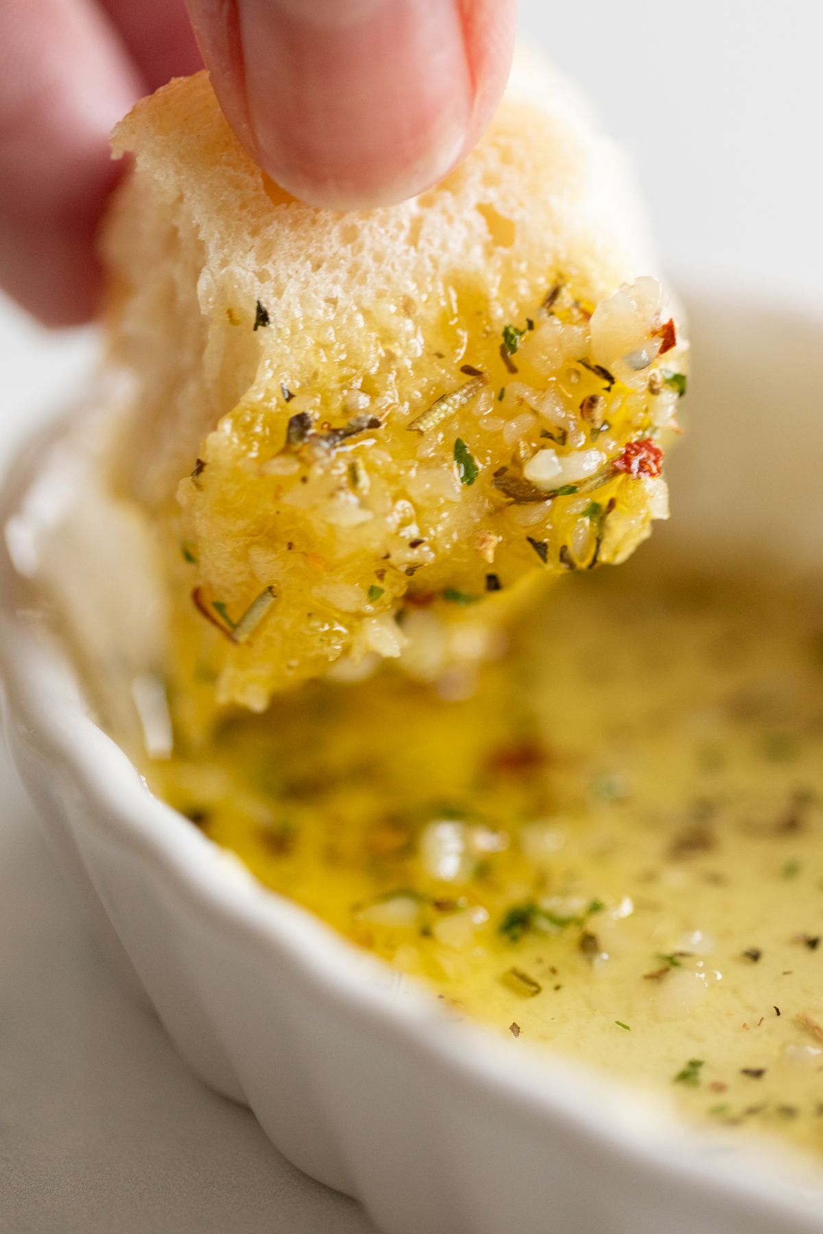 A hand dipping a piece of bread into a white ramekin full of olive oil bread dip.