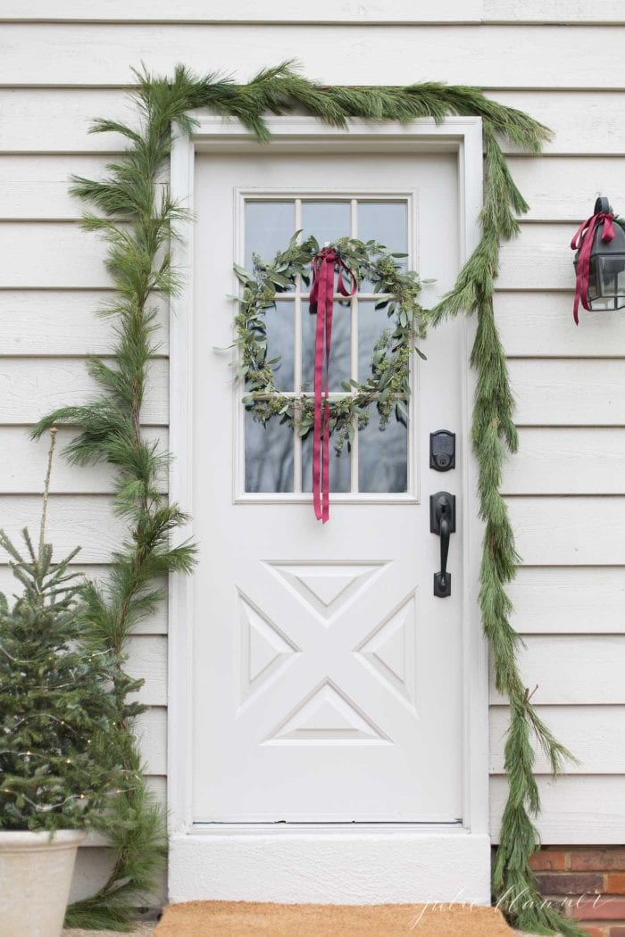 Front door with pine garland, eucalyptus wreath and mini Christmas tree