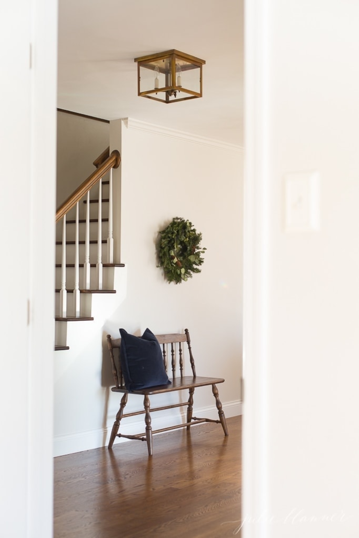A Christmas wreath placed over a wooden bench in the entryway of a home