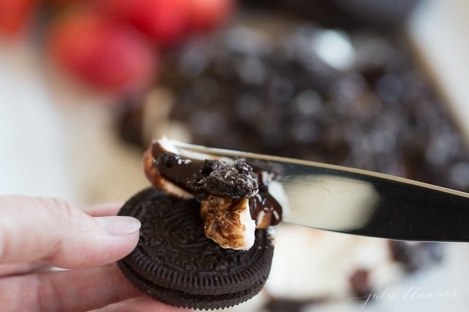 A knife spreading cookies and cream spread onto an oreo