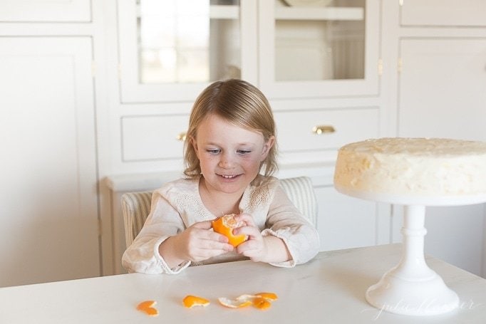 mandarin orange cake on stand, little girl to the side peeling oranges.