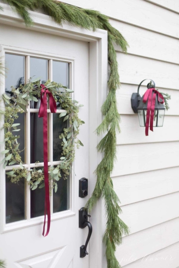A white exterior door surrounded by pine garlands