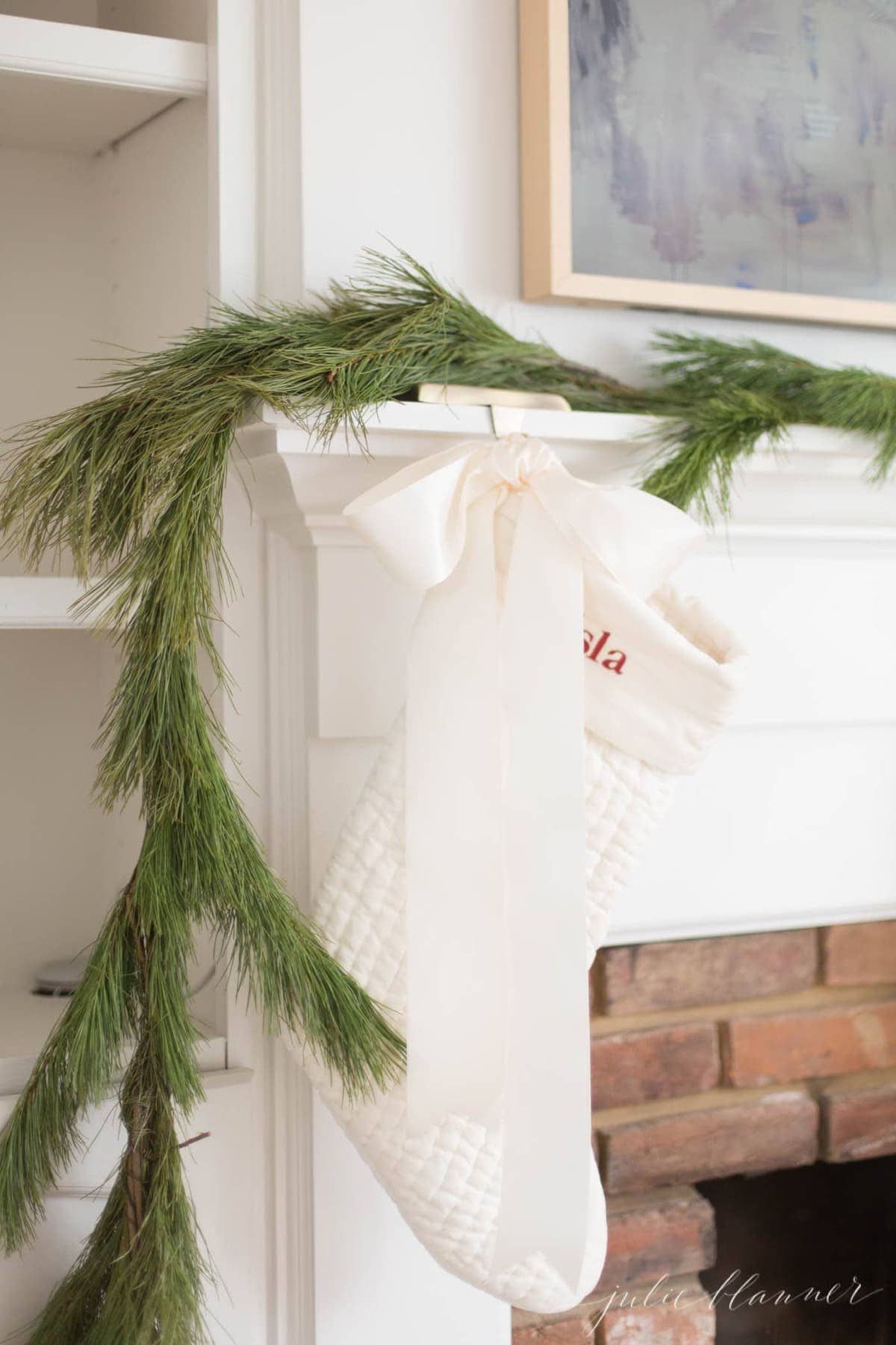 A brick fireplace with a white mantel and a greenery garland hung with stockings for christmas
