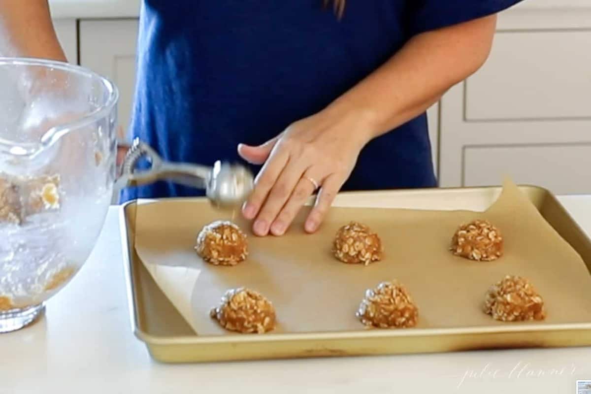 dropping oatmeal cookies on parchment lined cookie sheet with scoop