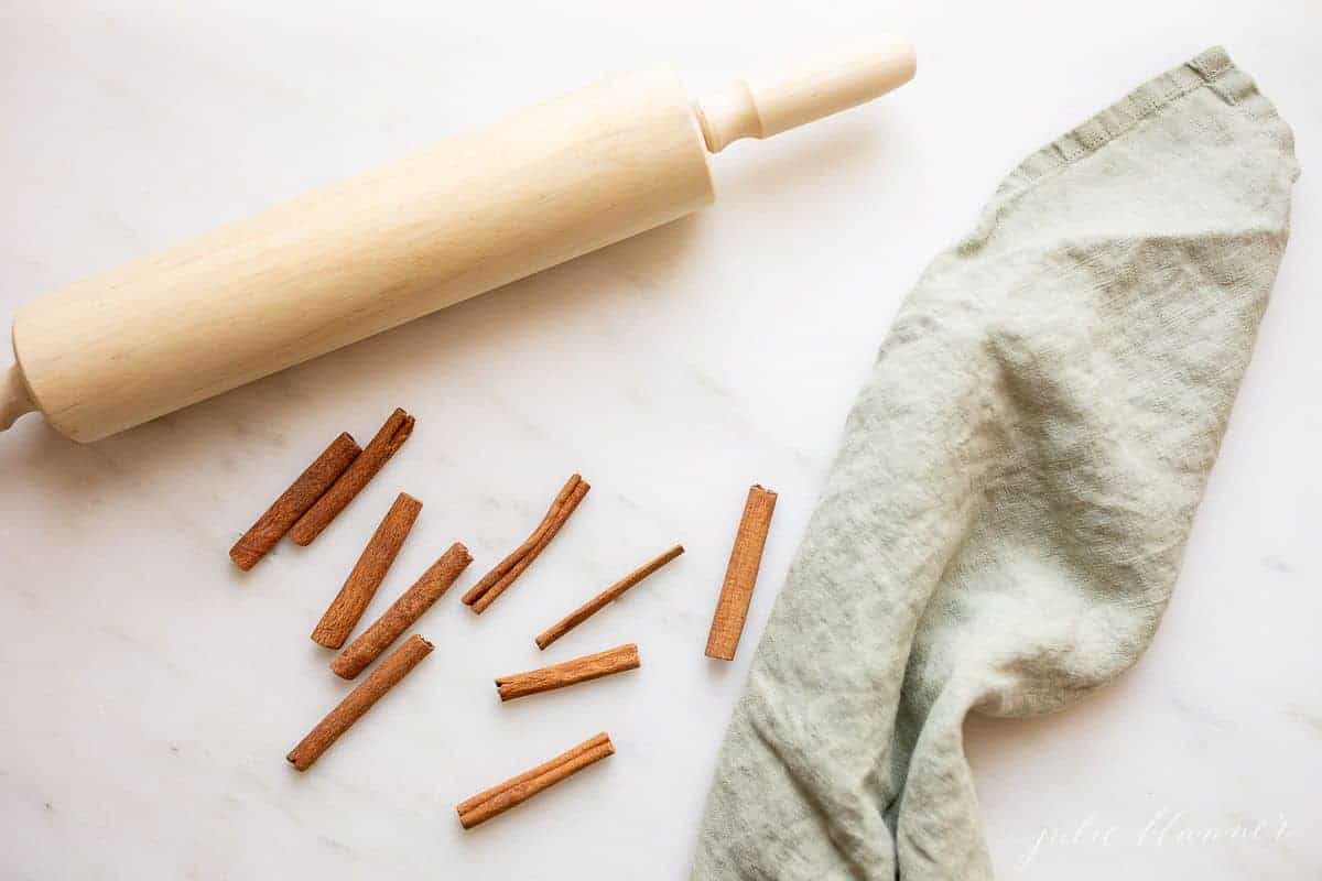 A wooden rolling pin on a marble surface, crushed cinnamon sticks and a linen towel.