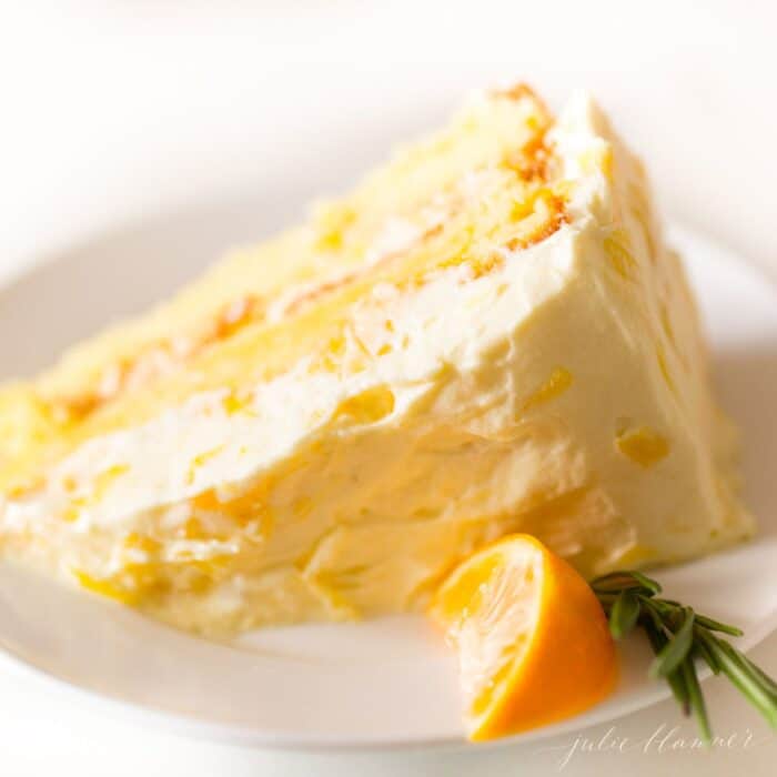 A slice of mandarin cake with an orange slice and a sprig of rosemary on the plate.