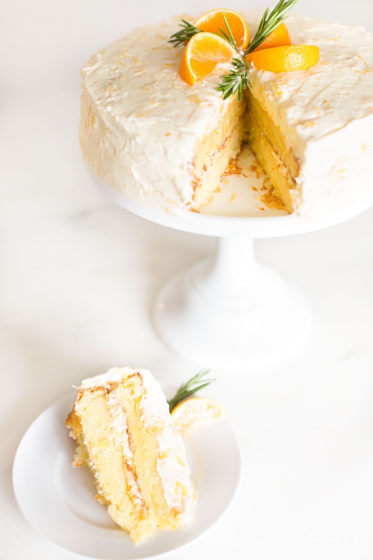 A mandarin orange cake on a cake stand, slice removed to a plate in front.