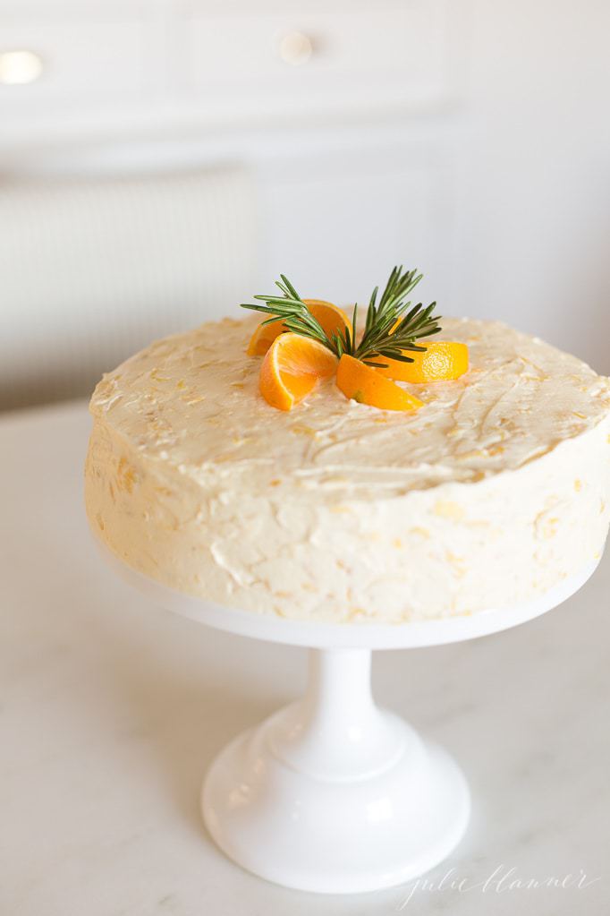 Mandarin Orange Cake topped with fresh mandarin slices and rosemary sprigs on a white platter.