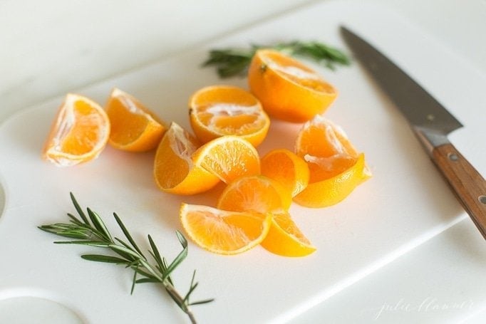 Slices of mandarin oranges and fresh rosemary on a white cutting board, knife to the side.