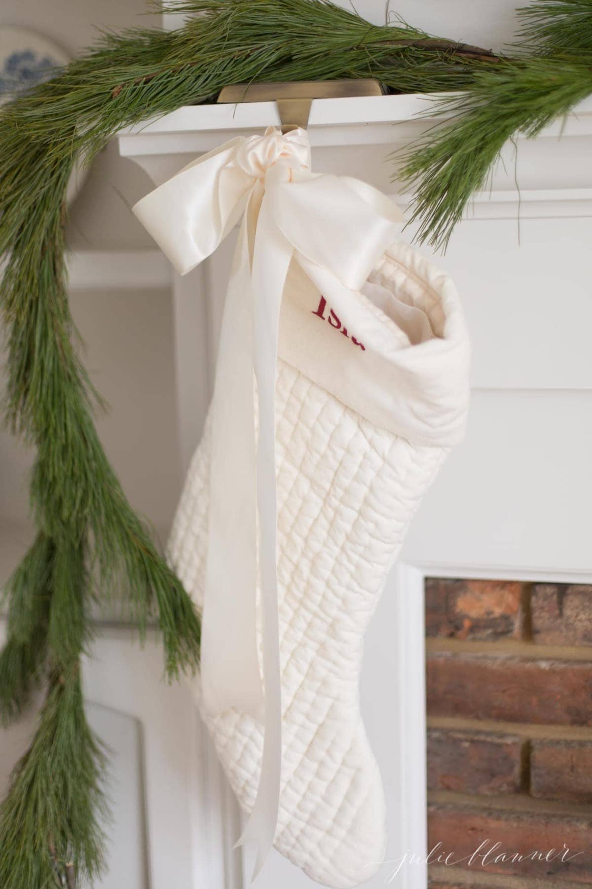 A brick fireplace with a white mantel and a greenery garland hung with stockings for christmas