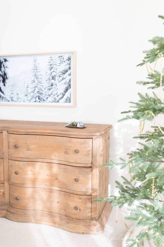 A Samsung art tv on the wall of a bedroom with a winter scene displayed, Christmas tree in foreground.
