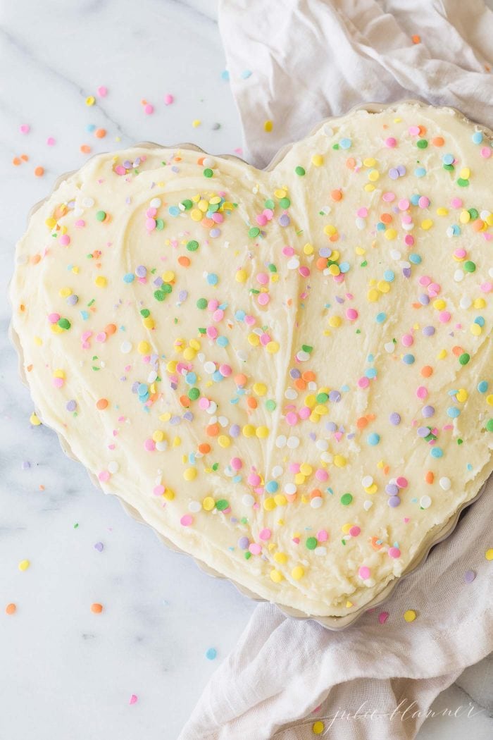 A heart shaped sugar cookie cake with frosting and sprinkles