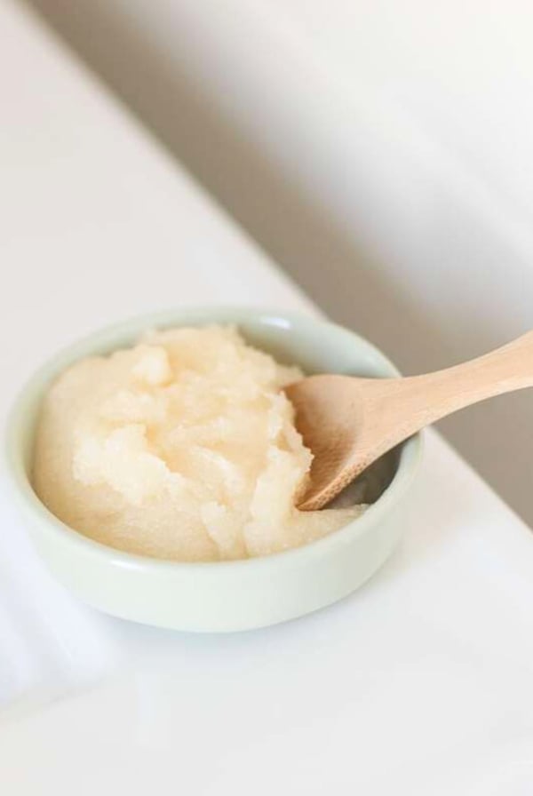 A homemade lip scrub recipe in a small container with a wooden spoon.