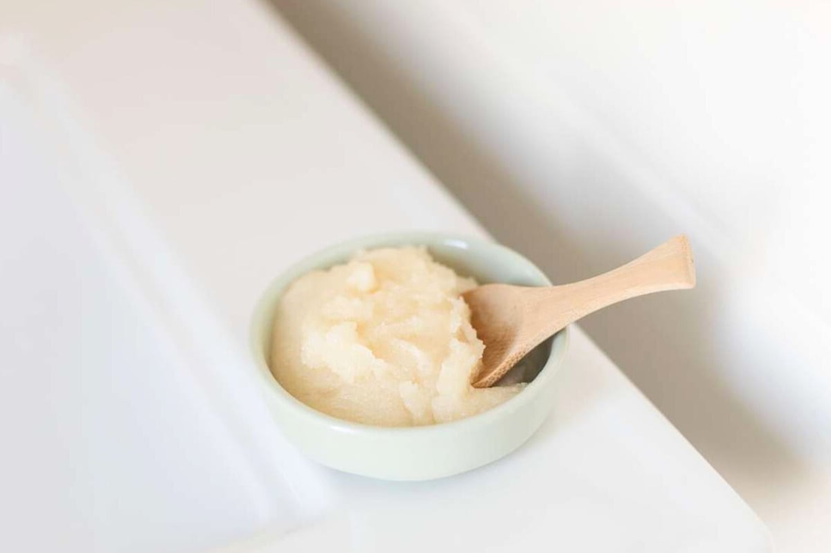 A homemade lip scrub recipe in a small container with a wooden spoon.