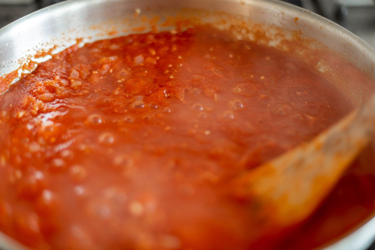 A tomato sauce cooking on a range, wooden spoon to the side.