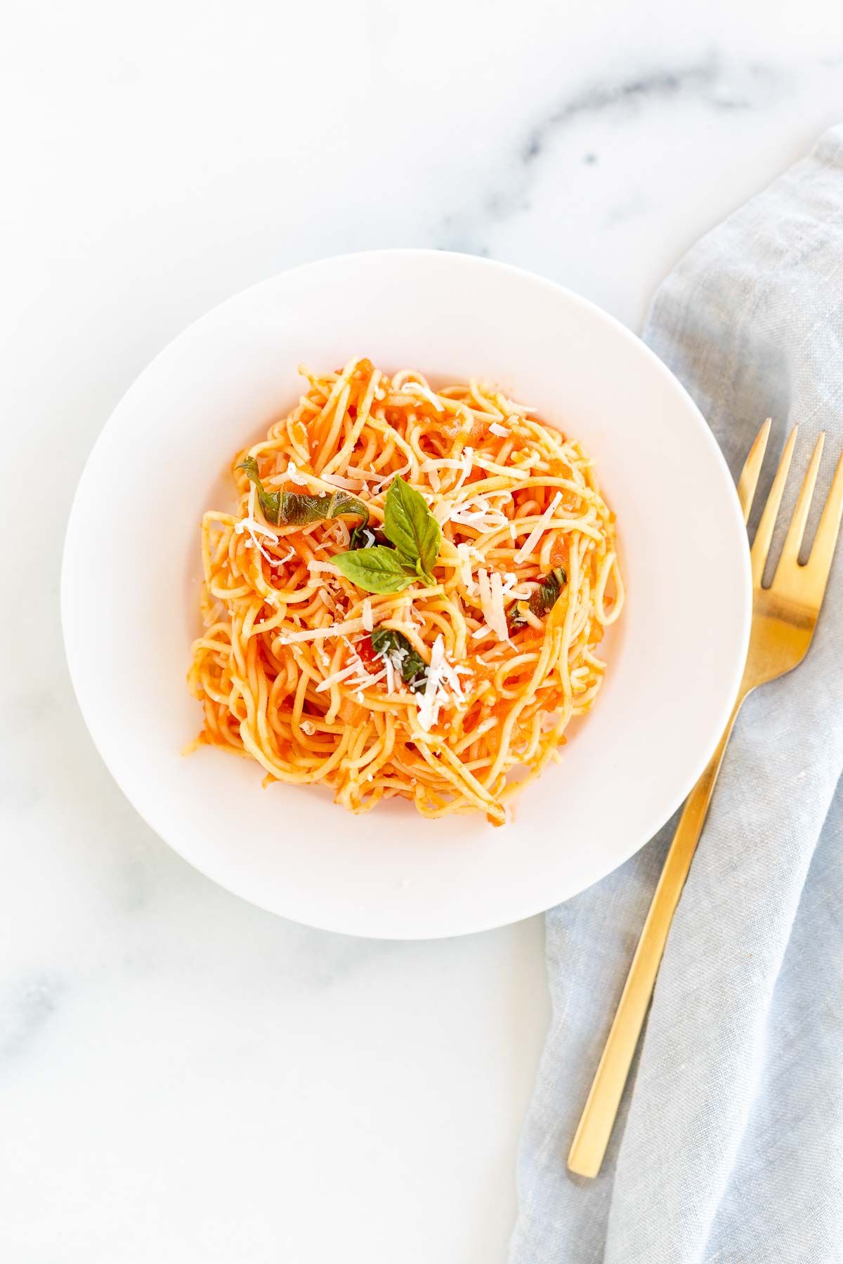 A white plate filled with pasta in a pomodoro sauce, gold fork to the side